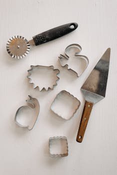 A top view of metal cake server, pizza cutter, and cookie cutters on a white background.